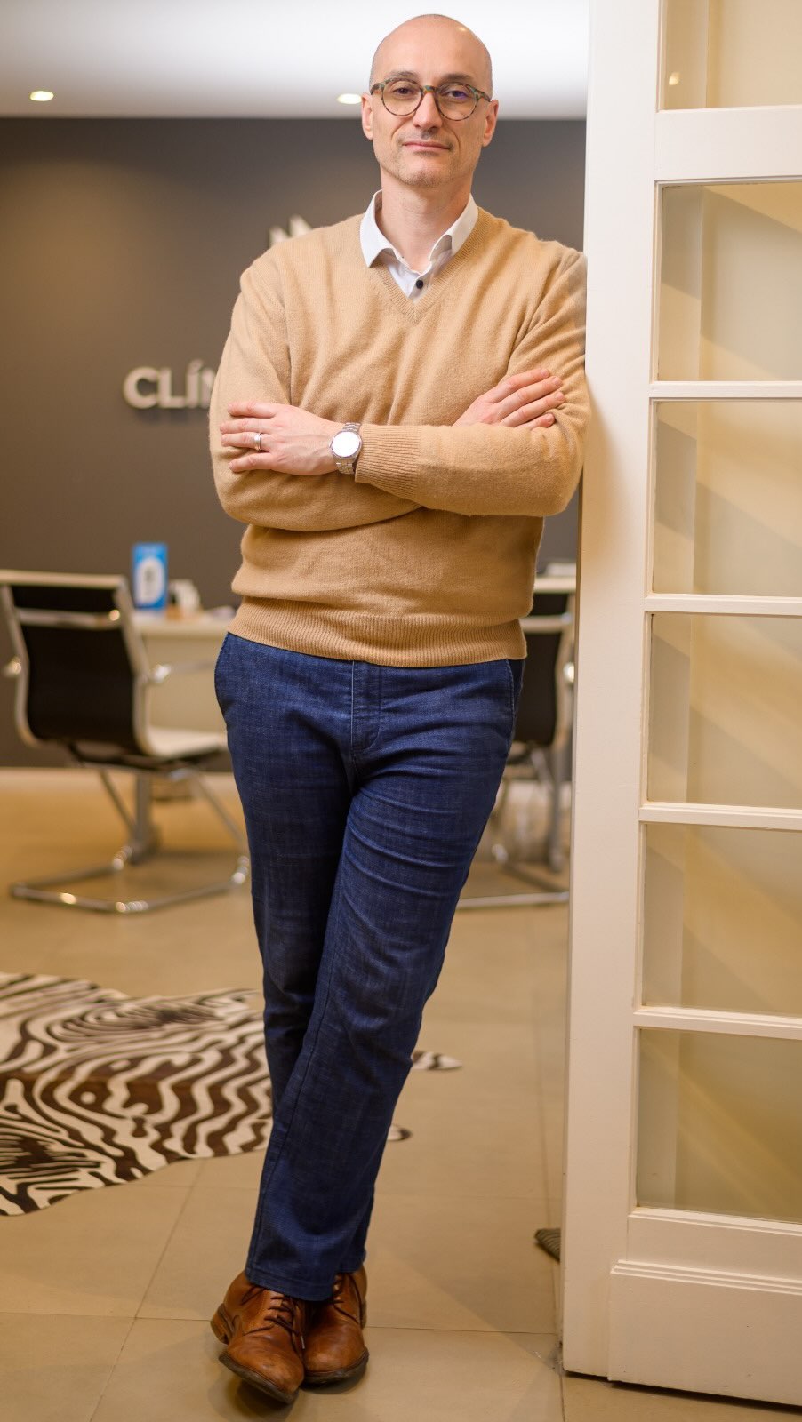 El Dr. Daniel Murillo apoyado en la puerta blanca de la recepción, con la pared grafito y el cartel de Clínica Murillo detrás